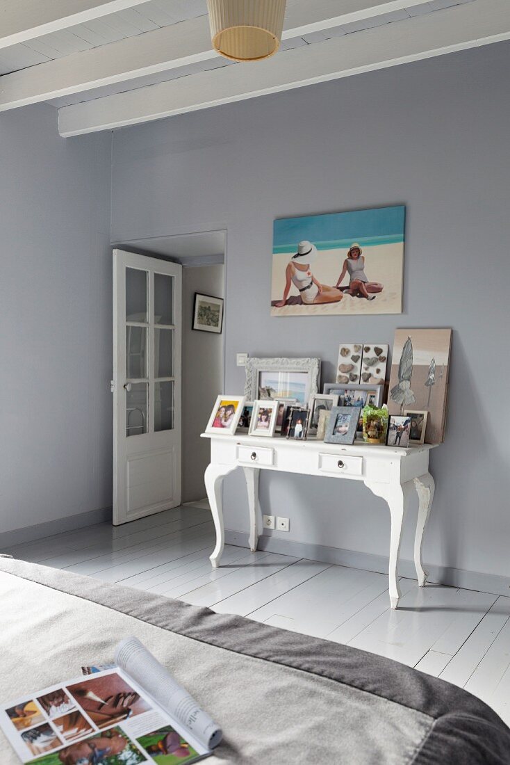 Schlafzimmer mit graublauem Dielenboden und Wänden, weißer Konsoltisch mit Bildern