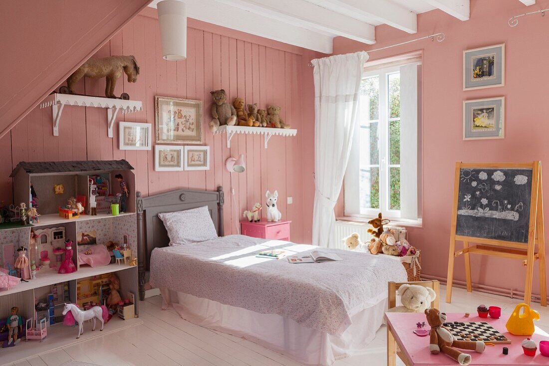 Nostalgisches Kinderzimmer mit rosafarbenen Wänden, einem großen Puppenhaus und Bett mit Volant