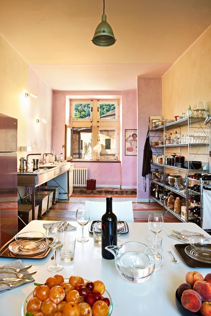 Simple, loft-apartment kitchen with open-fronted metal shelves, marbled walls in complementary colours and set table in foreground