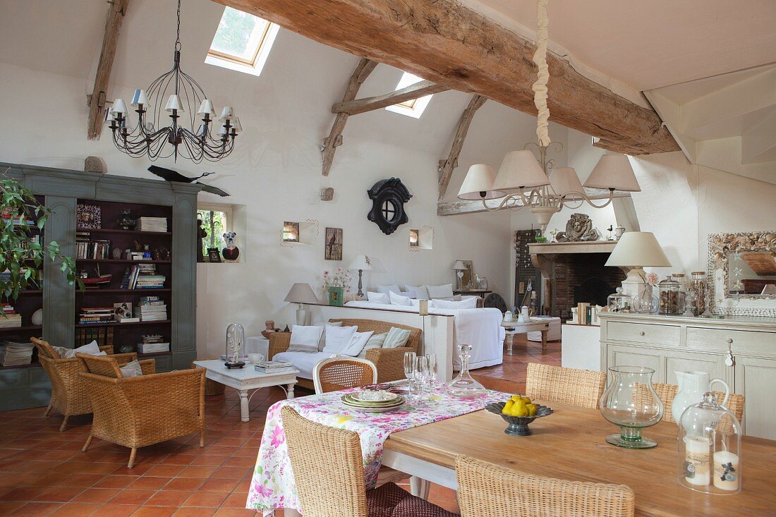 Exposed rustic wooden beams, dining area and wicker armchairs in lounge in open-plan interior