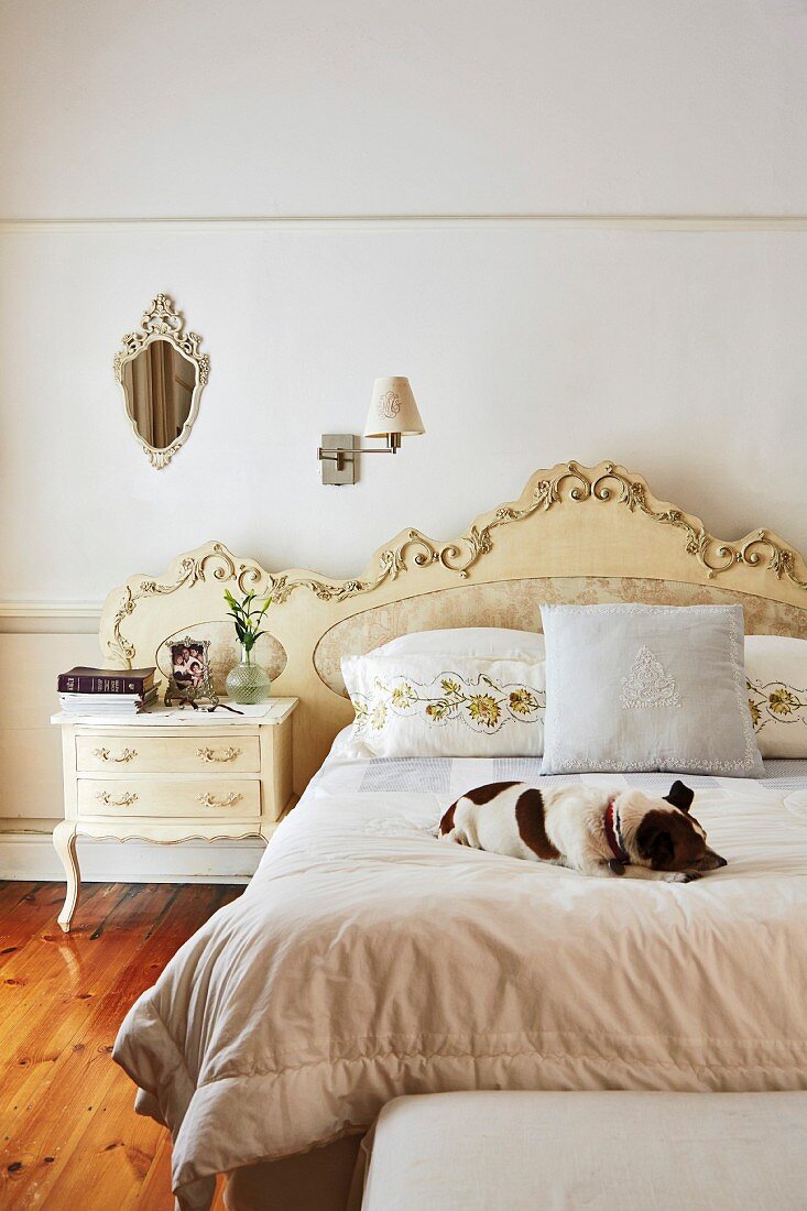 Hund auf Doppelbett, Kopfteil mit verspielter Goldverzierung, Nachtkästchen im Rokokostil und Vintage Wandleuchte