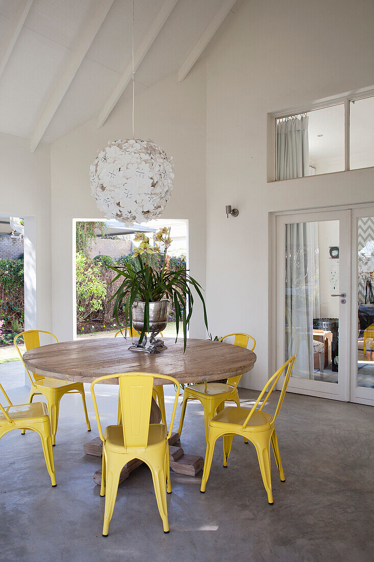 Bright dining area with round wooden table and yellow metal chairs
