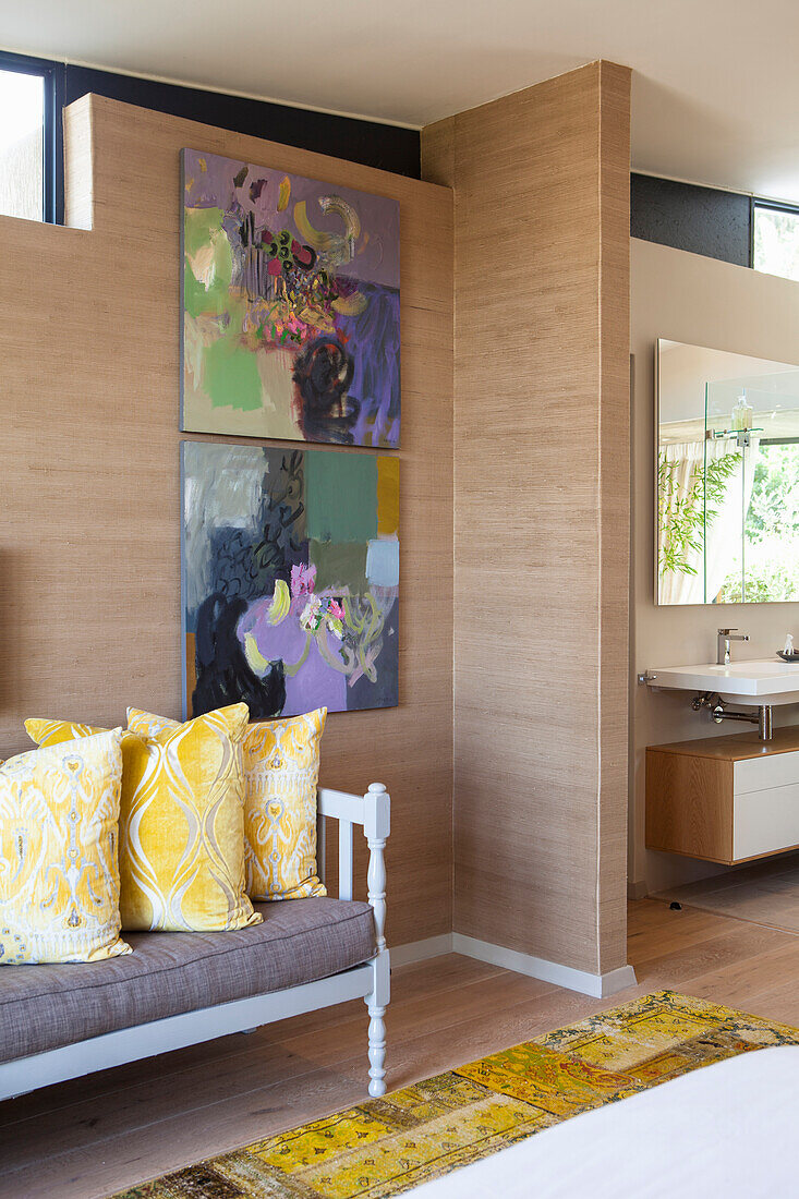 Bedroom with artwork on the wall, yellow accent cushions and view of the bathroom