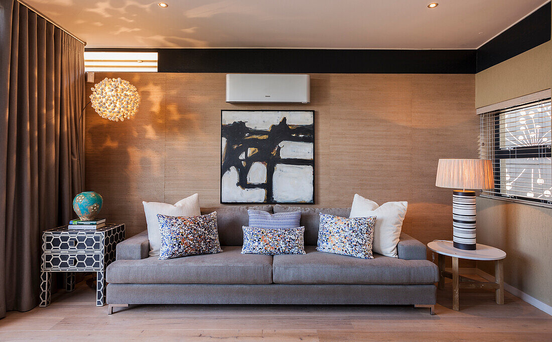 Wohnzimmer mit grauem Sofa, abstraktem Wandbild und Tischlampe