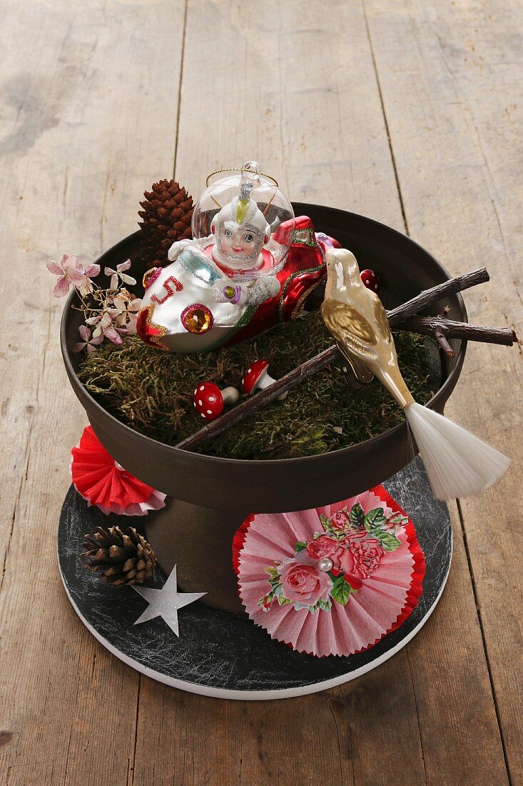 Arrangement of Christmas decorations and moss in black dish and hand-crafted paper rosette on plate