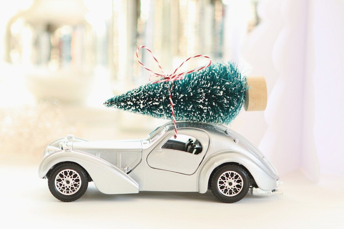 Spielzeugauto mit Weihnachtsbäumchen auf Autodach vor unscharfem Hintergrund