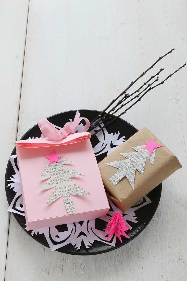 Selbstgemachte rosa Papiertüte und Geschenk mit ausgeschnittenen Tannenbäumchen beklebt, auf Teller mit Papierdeckchen und kleiner Rute