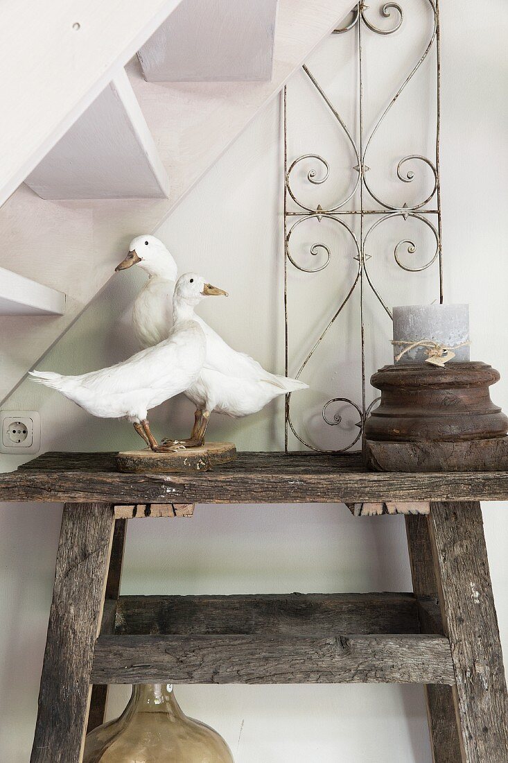 Stuffed geese and candle in wooden candle holder on rustic wooden table below staircase