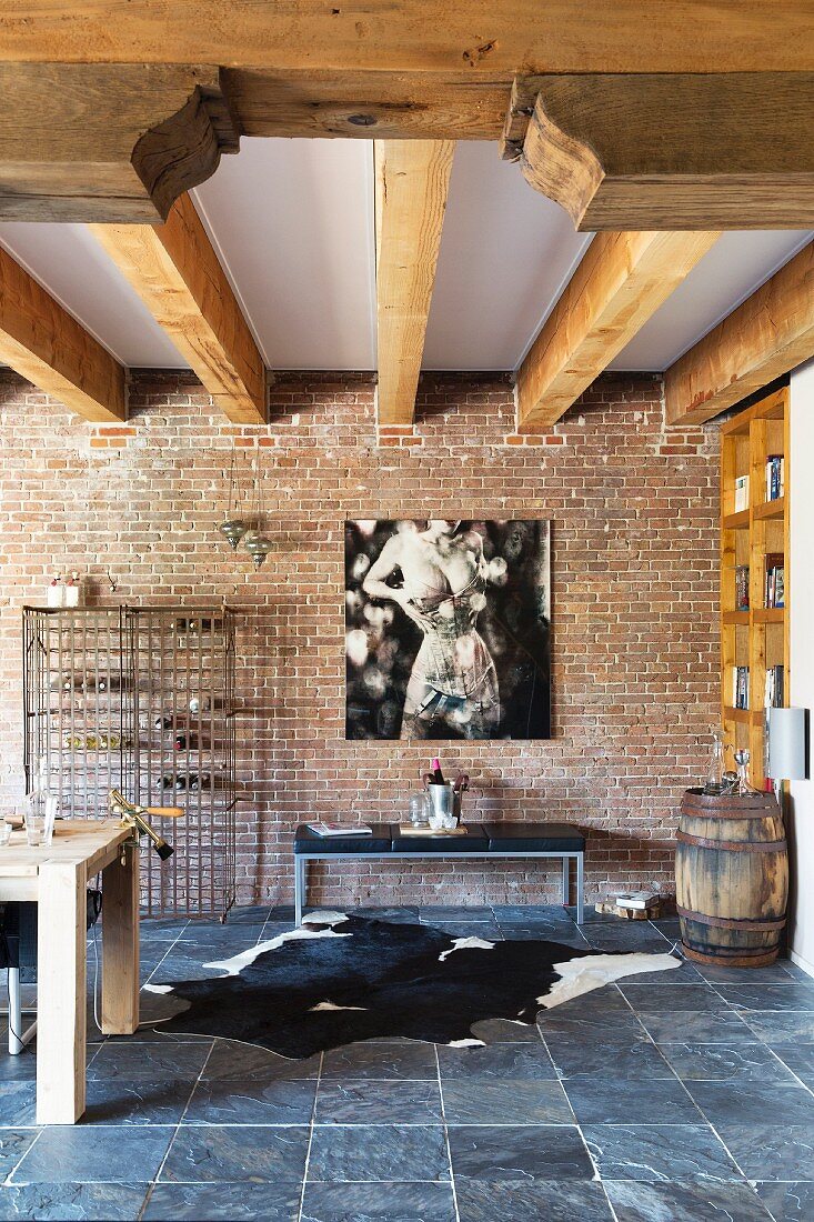 Loft-Wohnung mit Holzbalkendecke und Backseinwand, grossformatiges Foto, Sitzbank und Tierfell auf grauem Schieferboden