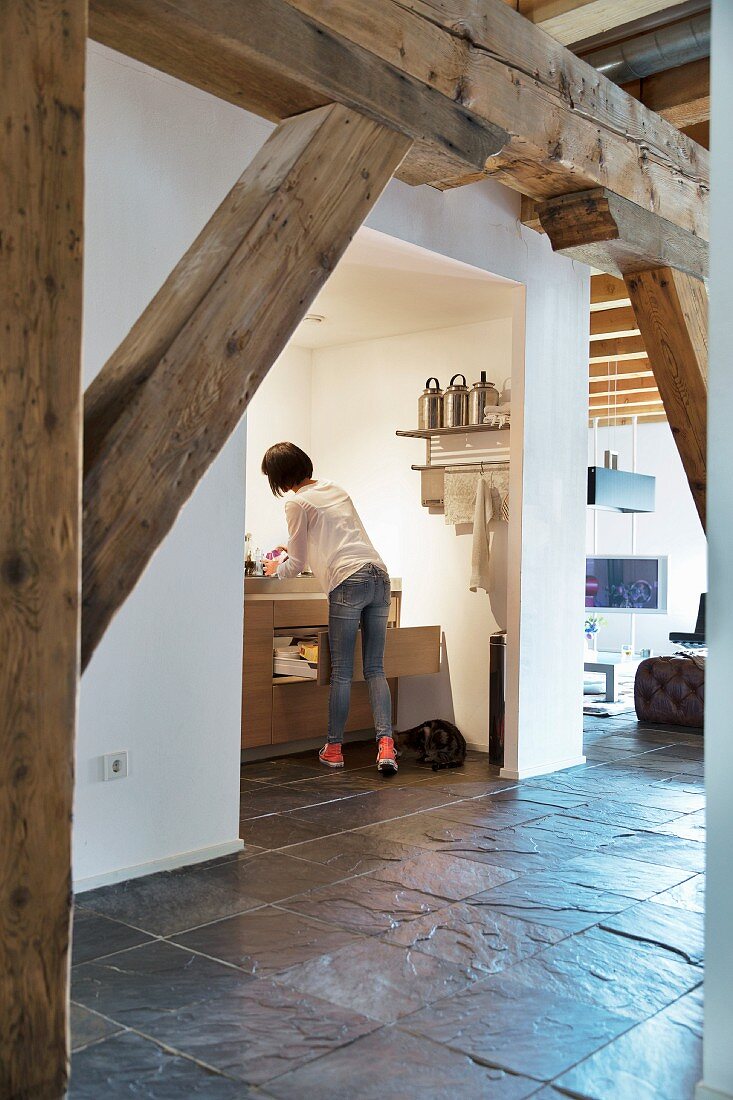 Exposed wooden beams and slate floor in loft apartment with woman in kitchen in background
