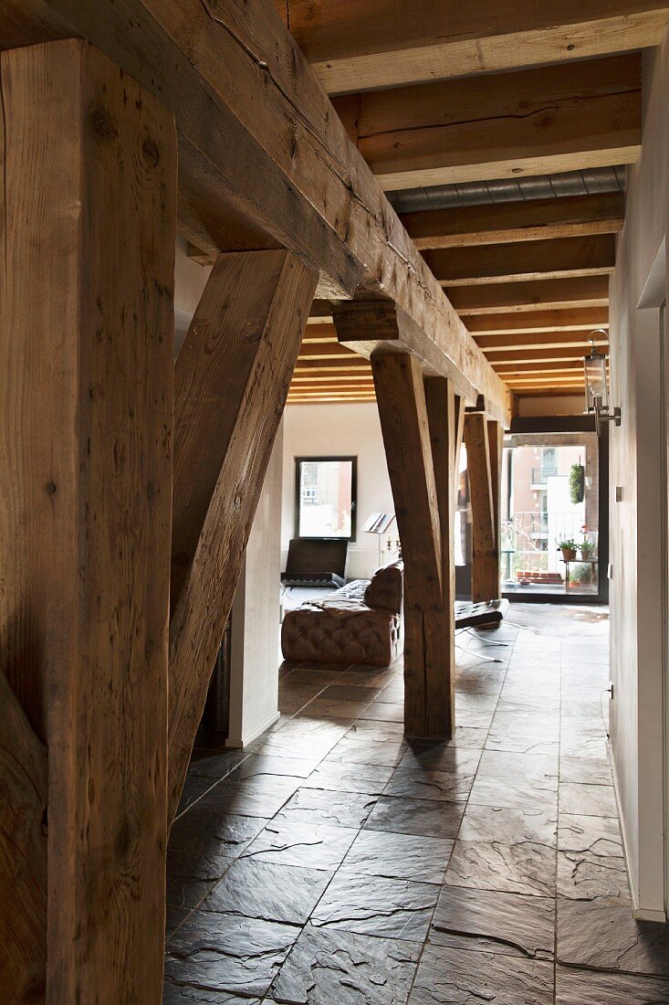 Rustikale Tragwerkkonstruktion aus Holz unter Holzbalkendecke in Loft-Wohnung mit Schieferboden