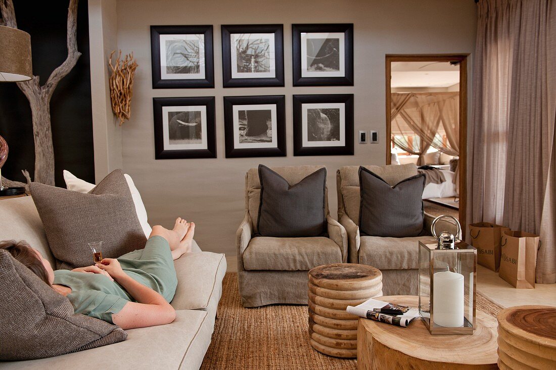 Woman lying on couch and tree-stump coffee tables in living room in various natural shades