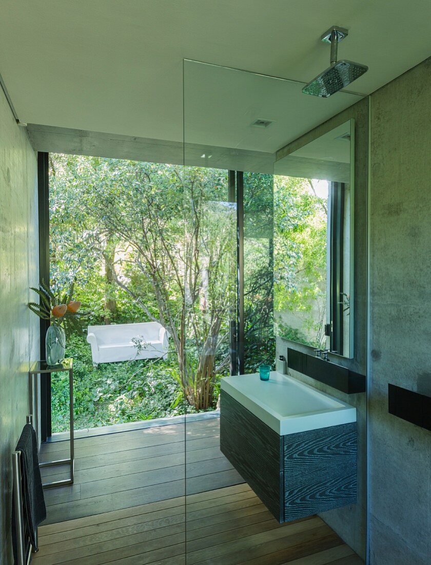 Designerbad mit begehbarer Dusche, Blick durch Glasfront auf weisses Outdoor-Sofa im Garten