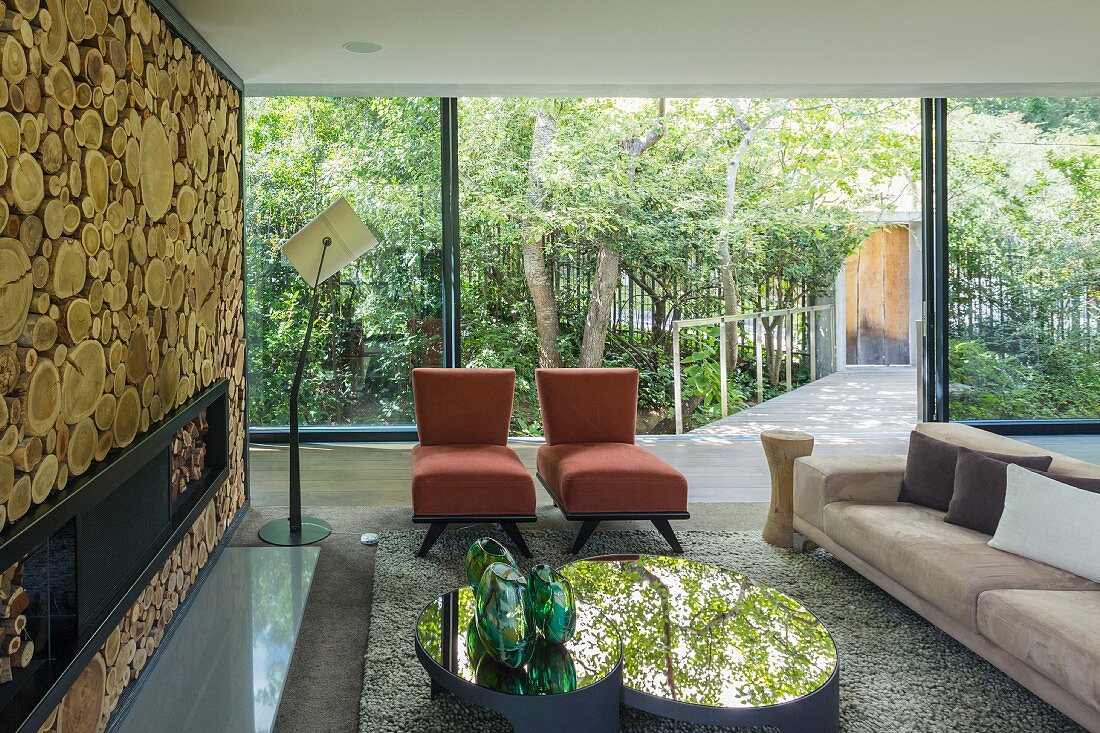 Designersofa, Long-Sessel und spiegelnde Coffeetable vor Kaminwand aus Holzstämmen