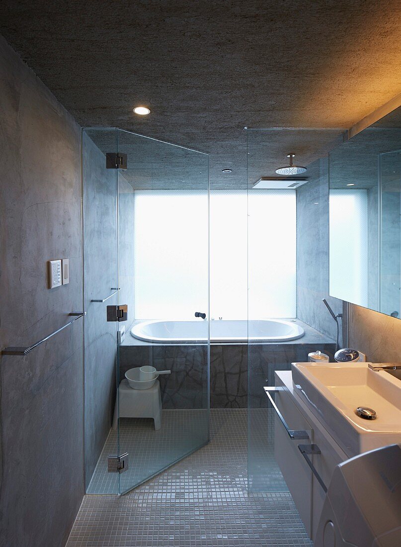 Badezimmer in japanischem Betonhaus mit Wanne und begehbarer Dusche hinter Glastrennwand, Waschtisch im Vordergrund