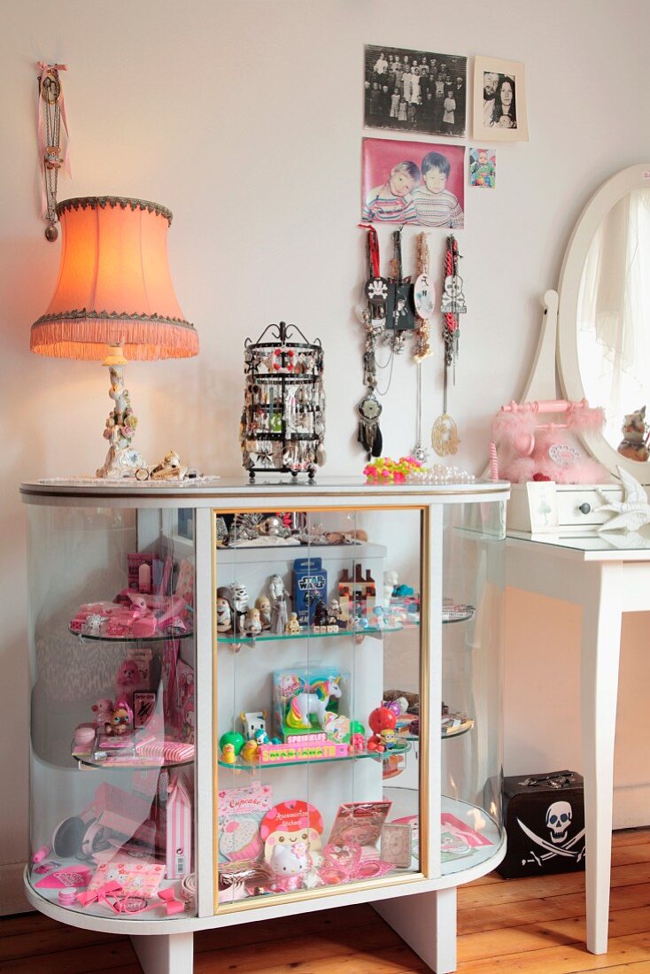 Mit rosarotem Spielzeug, Schmuck und Tischleuchte dekorierte Vitrine in romantischem Mädchenzimmer