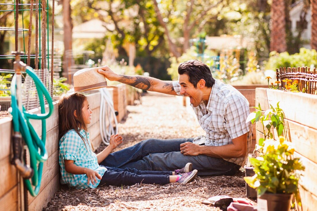 Vater und Tochter sitzen neben Hochbeet im Garten