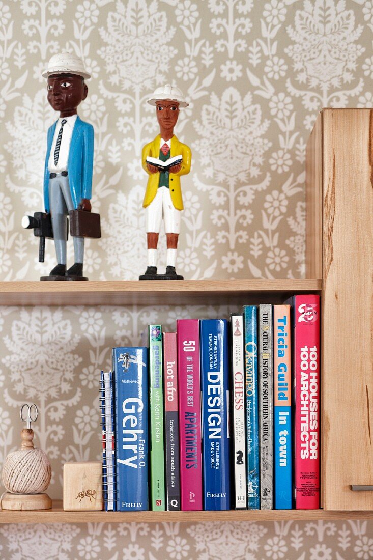 Wallpaper with pale pattern behind figurines and books on wall-mounted shelves