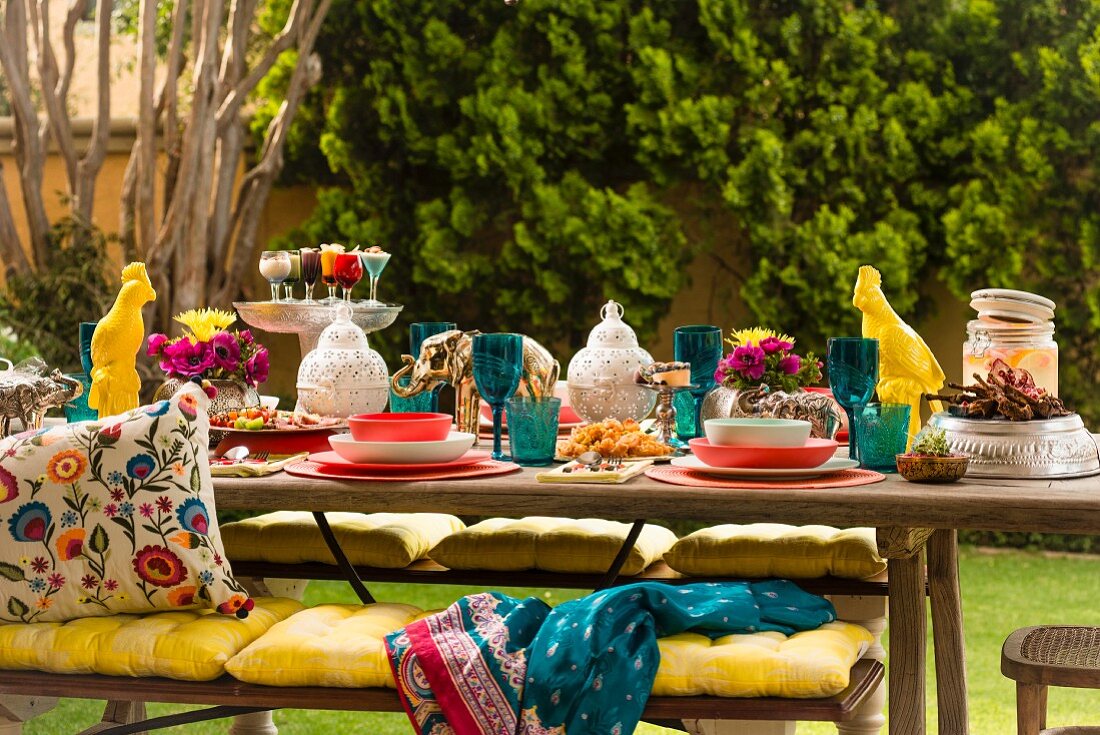 Colourful, set table with lanterns, animal figurines, yellow seat cushions on bench and ethnic scatter cushions