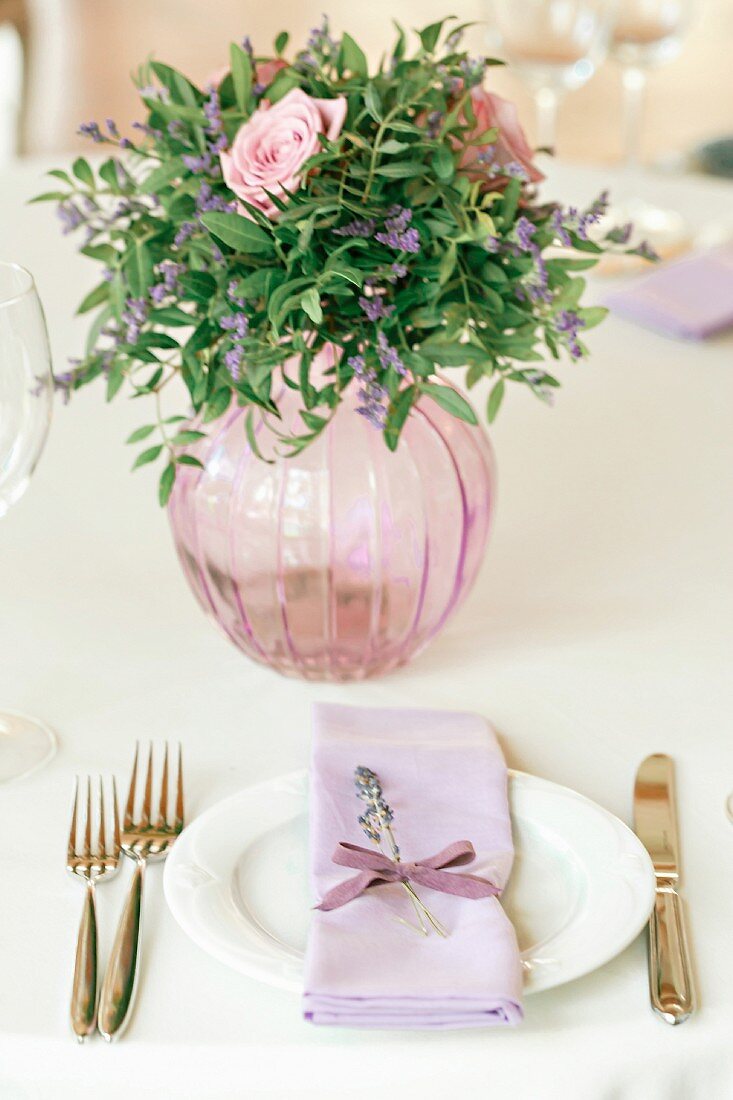 Romantic flower arrangement in glass vase and festive place settling with lilac napkin