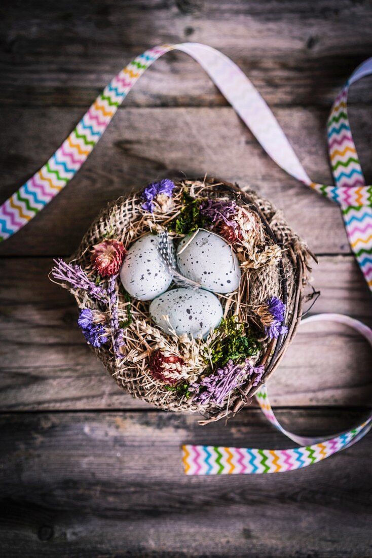 Hellblaue Ostereier in Körbchen mit Strohblumen und Geschenkband