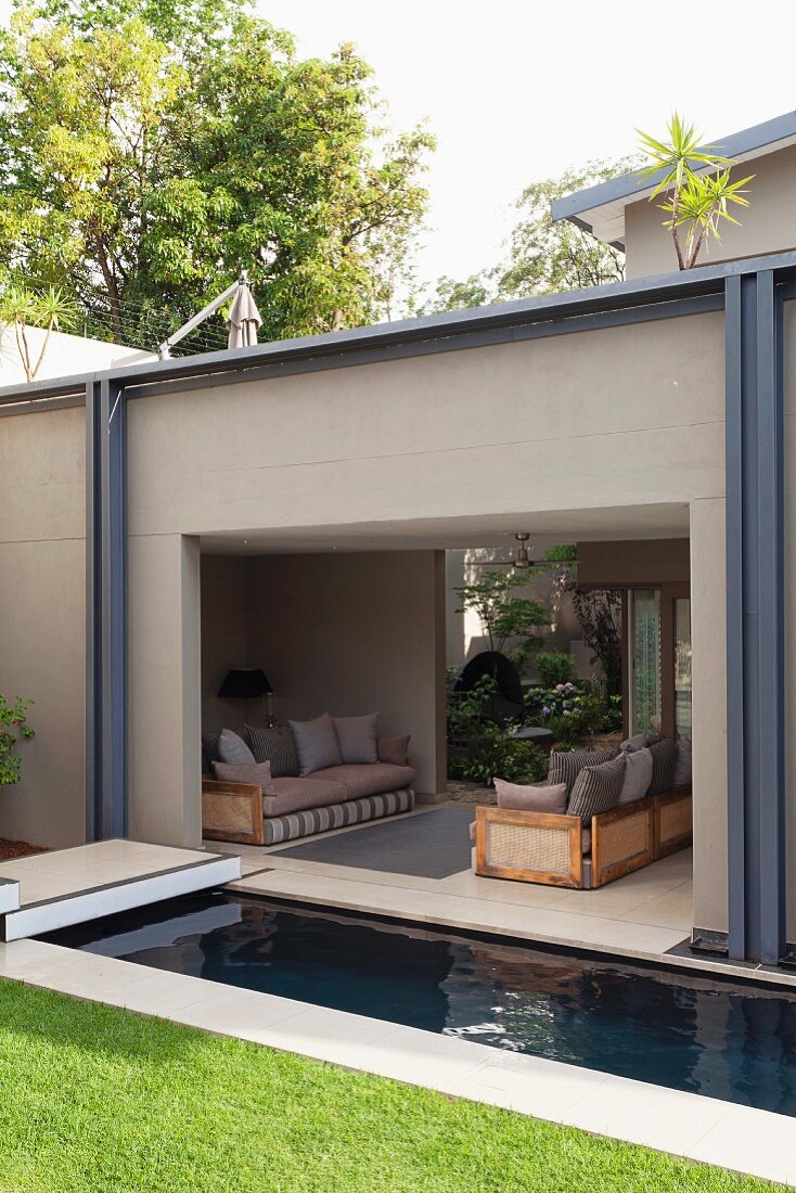 Narrow pool between lawn and open-sided seating area with sofas