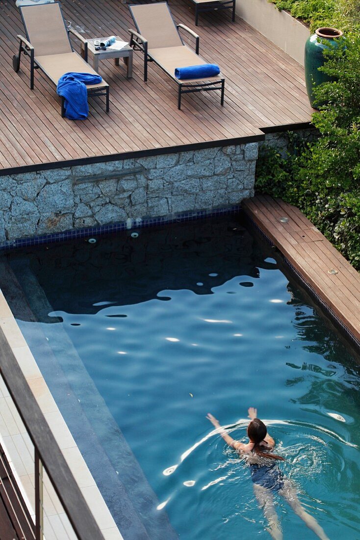 Woman swimming in pool below wooden deck with sun loungers