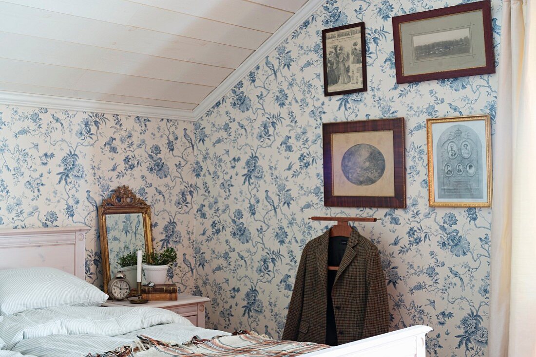 Schlafzimmer im Dachgeschoss mit floraler Tapete, alte gerahmte Fotos über stummem Diener