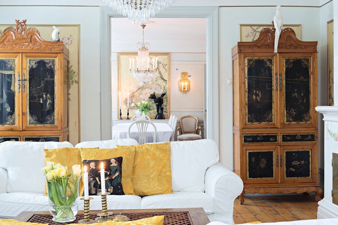 White sofa, antique cupboards with carved and painted panels in living room with view in to dining room through open doorway