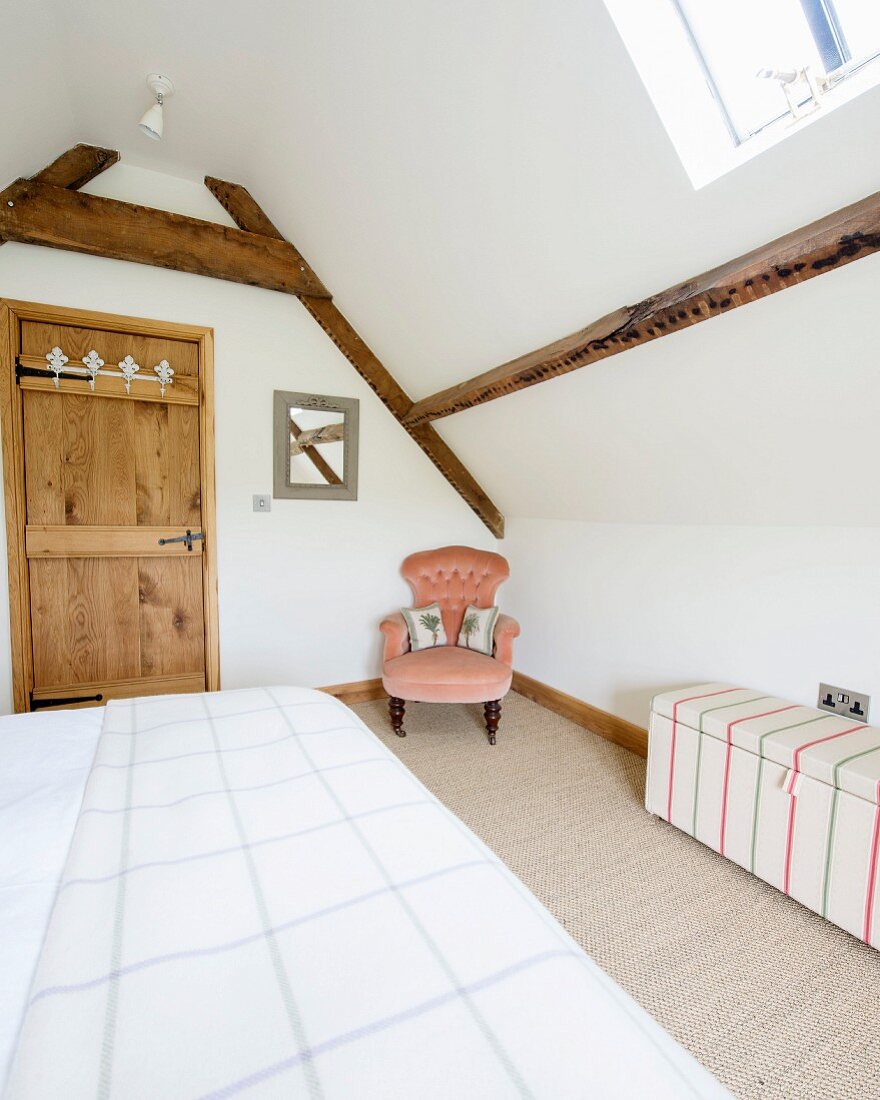 Doppelbett im Schlafzimmer mit Holzbalkenkonstruktion, zierlicher Polstersessel in Zimmerecke