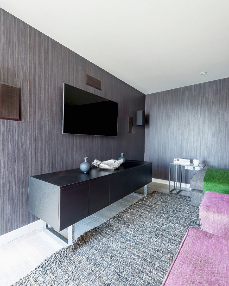 Schwarzes Sideboard unter Flachbildfernseher an graubraun gestreifter Tapete an Wand in modernem Wohnraum