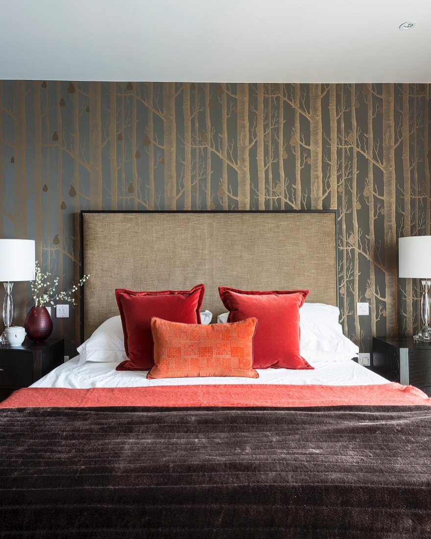 Drapierte Kissen auf Doppelbett mit hohem Kopfteil, vor tapezierter Wand mit Birkenwaldmotiv
