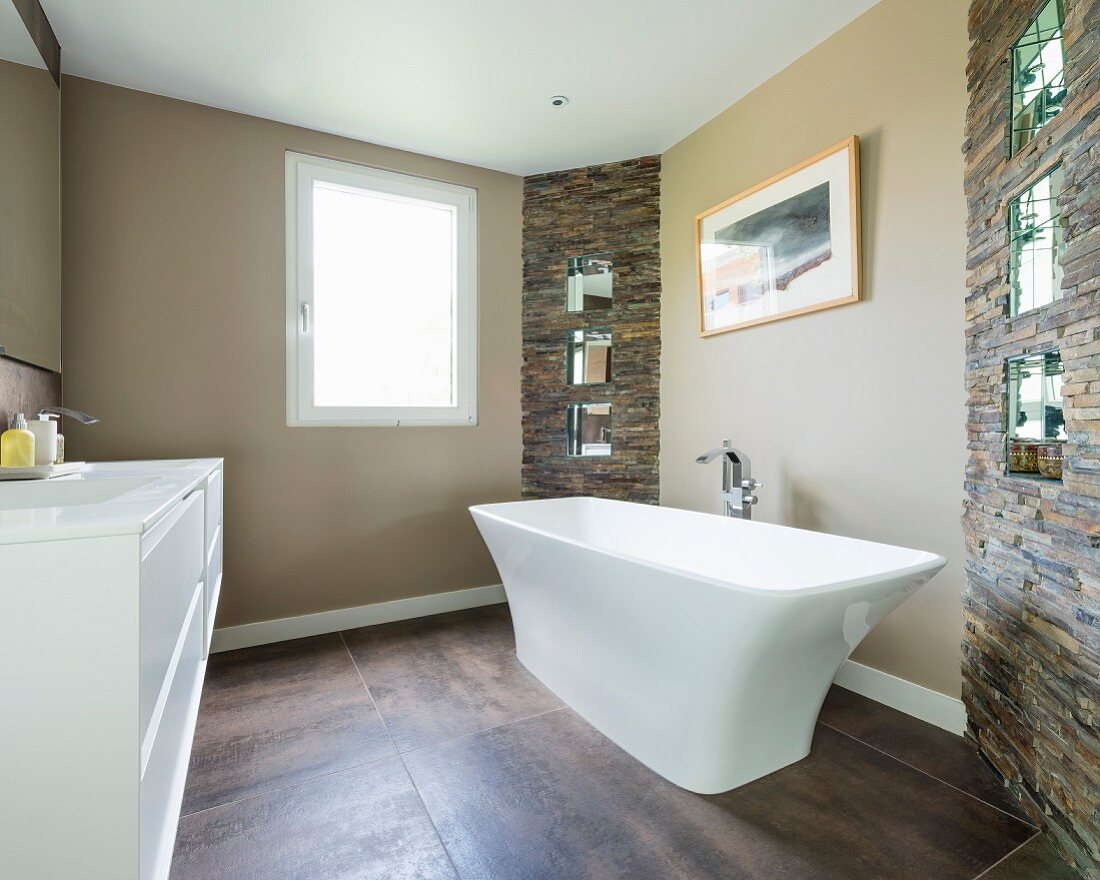 Freistehende Badewanne auf grossformatigem Fliesenboden in modernem Bad mit Naturstein Wandelementen