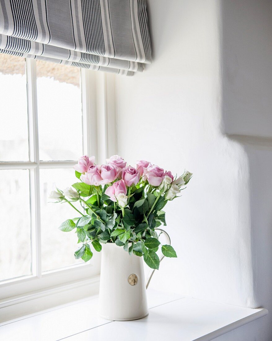 White jug of pink roses on windowsill
