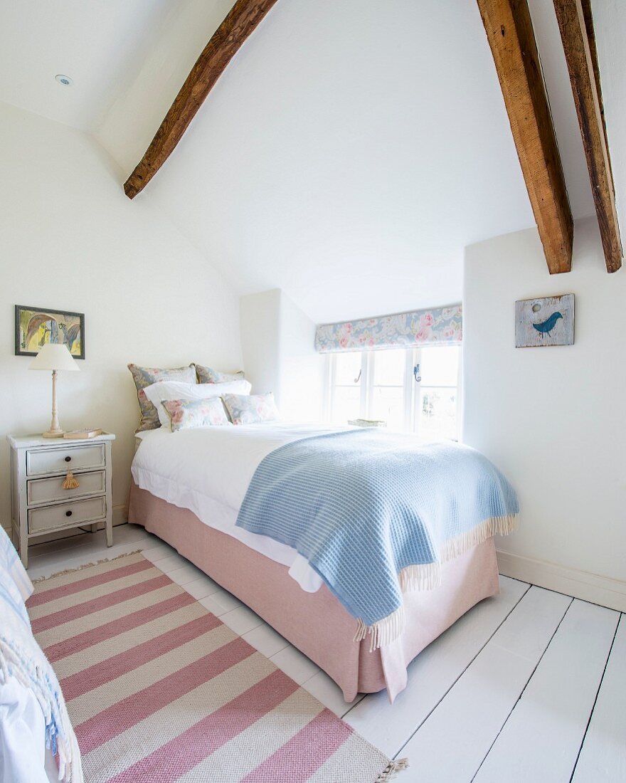 Einzelbett in Zimmerecke vor Fenster in ländlichem Schlafzimmer, rosa-weiss gestreifter Tepppichläufer auf weißem Dielenboden