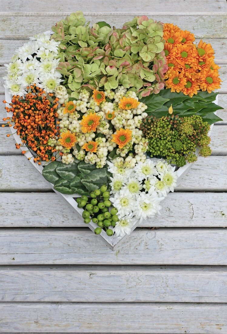 Hand-made, heart-shaped arrangement of chrysanthemums, hydrangeas and berries on wooden surface