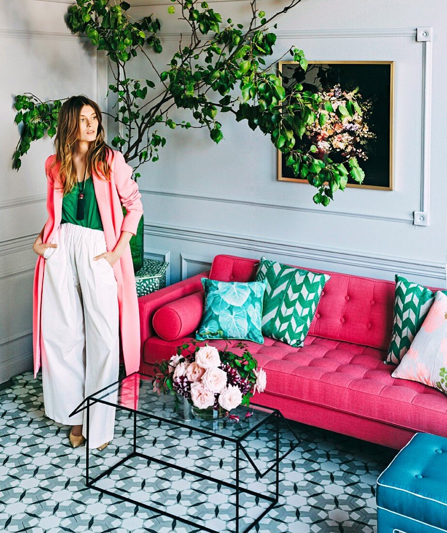 Junge Frau in Wohnraum mit pinkfarbenem Sofa, Glastisch, Fliesenboden und Zitronenbaum