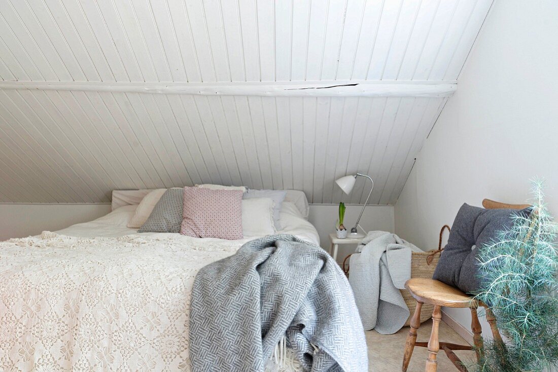 Doppelbett mit Spitzen-Tagesdecke unter Dachschräge mit weisser Holzverschalung