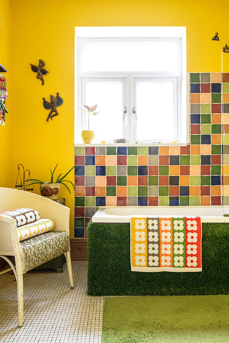 Bathtub clad with artificial grass against yellow wall and multicoloured tiles