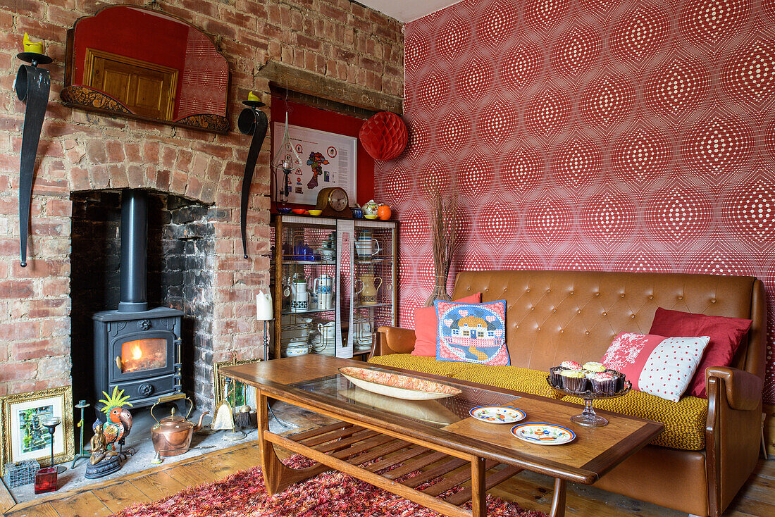 Coffee table and brown leather sofa against red wallpaper and log burner in fireplace in brick wall