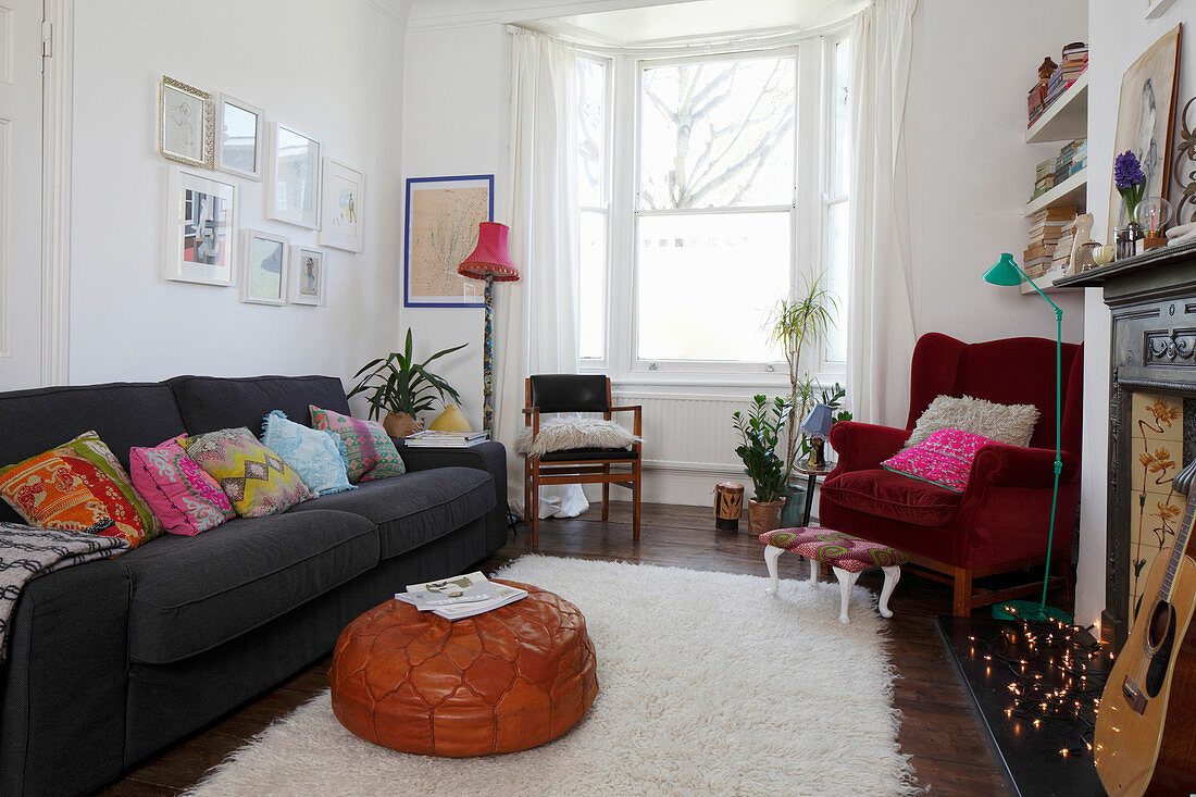 Graues Sofa mit bunten Kissen und roter Samtsessel im Wohnzimmer