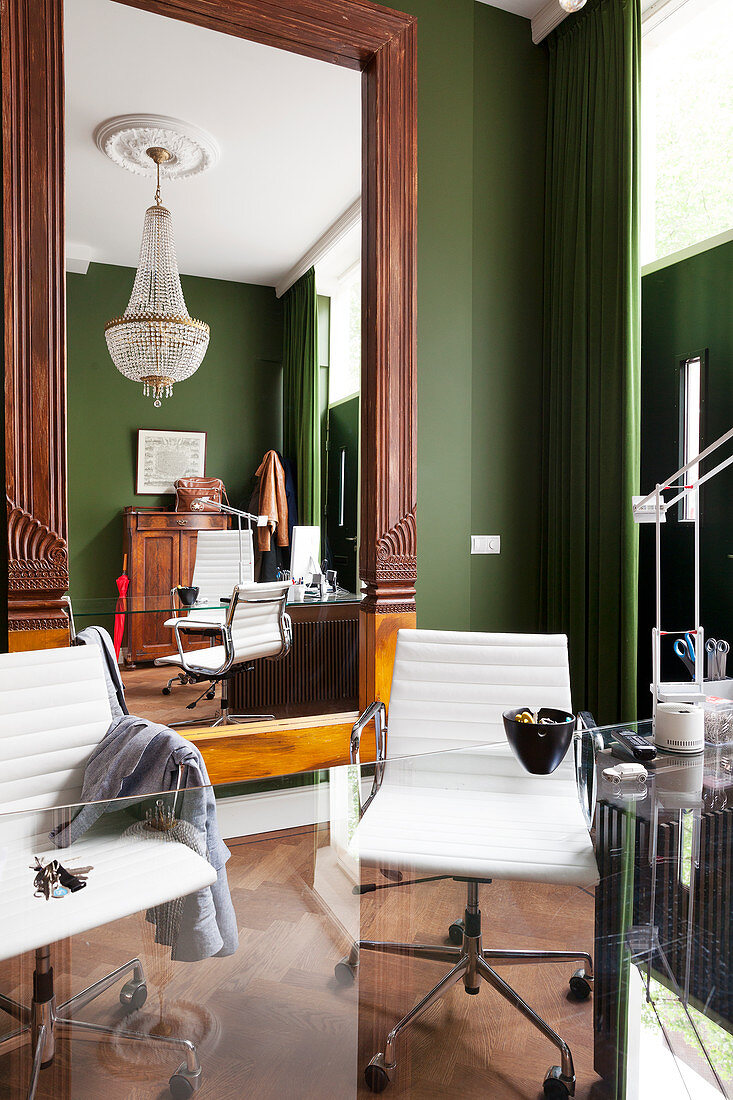 Klassikerstühle mit weißem Lederbezug hinter Glastisch, an grün getönter Wand grosser Wandspiegel mit geschnitztem Holzrahmen