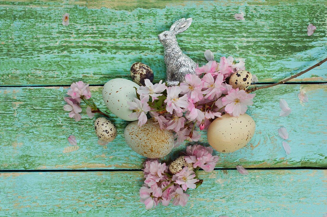Easter nest with cherry blossom, Easter eggs, quail's eggs and silver Easter bunny on wooden surface