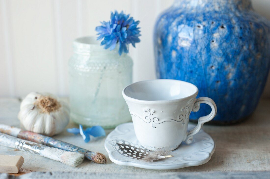 Blaue, antike Vase und verzierte Tasse, Pinseln und Blüte im Glas