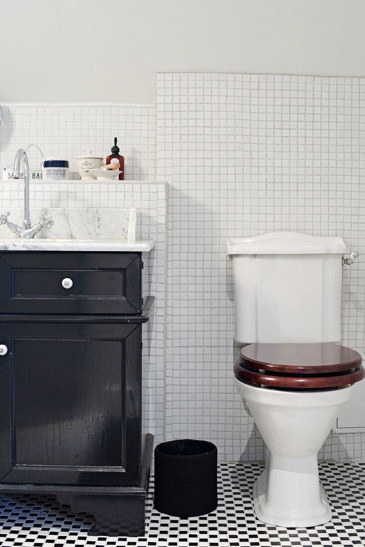 Toilet on black and white tiled floor next to black-painted washstand cabinet