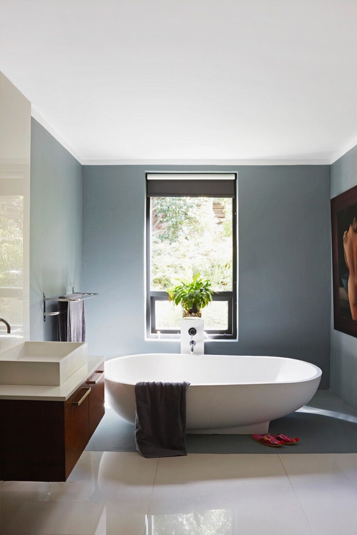Free-standing bathtub, mid-grey walls and section of floor and polished white floor tiles in elegant bathroom