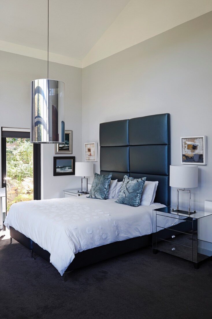 Double bed with tall, black-upholstered headboard and cylindrical pendant lamp in elegant bedroom