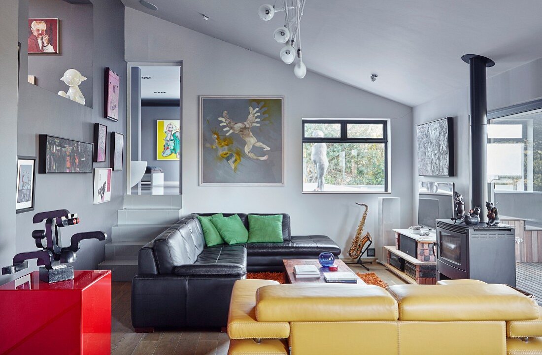 Schwarzes und gelbes Ledersofa in offenem Wohnraum mit grauen Wänden und Bildergalerie in künstlerischem Ambiente