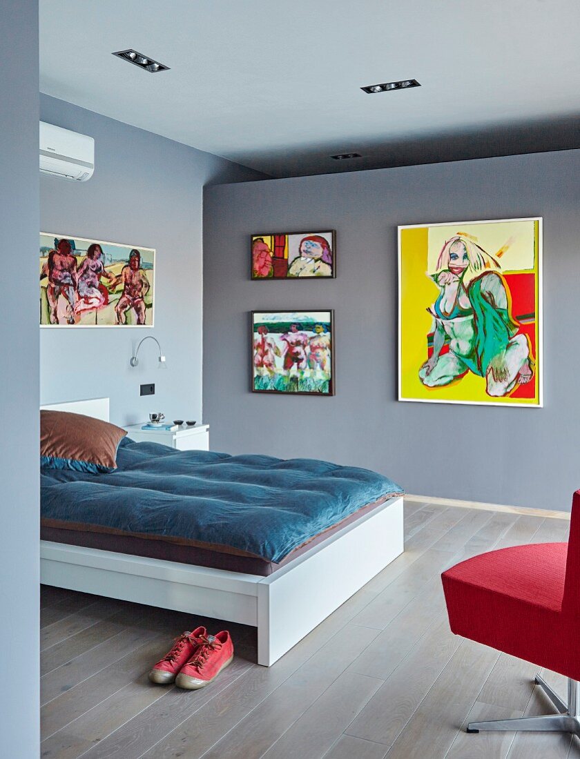 Double bed and gallery of modern paintings on wall of bedroom painted blue-grey