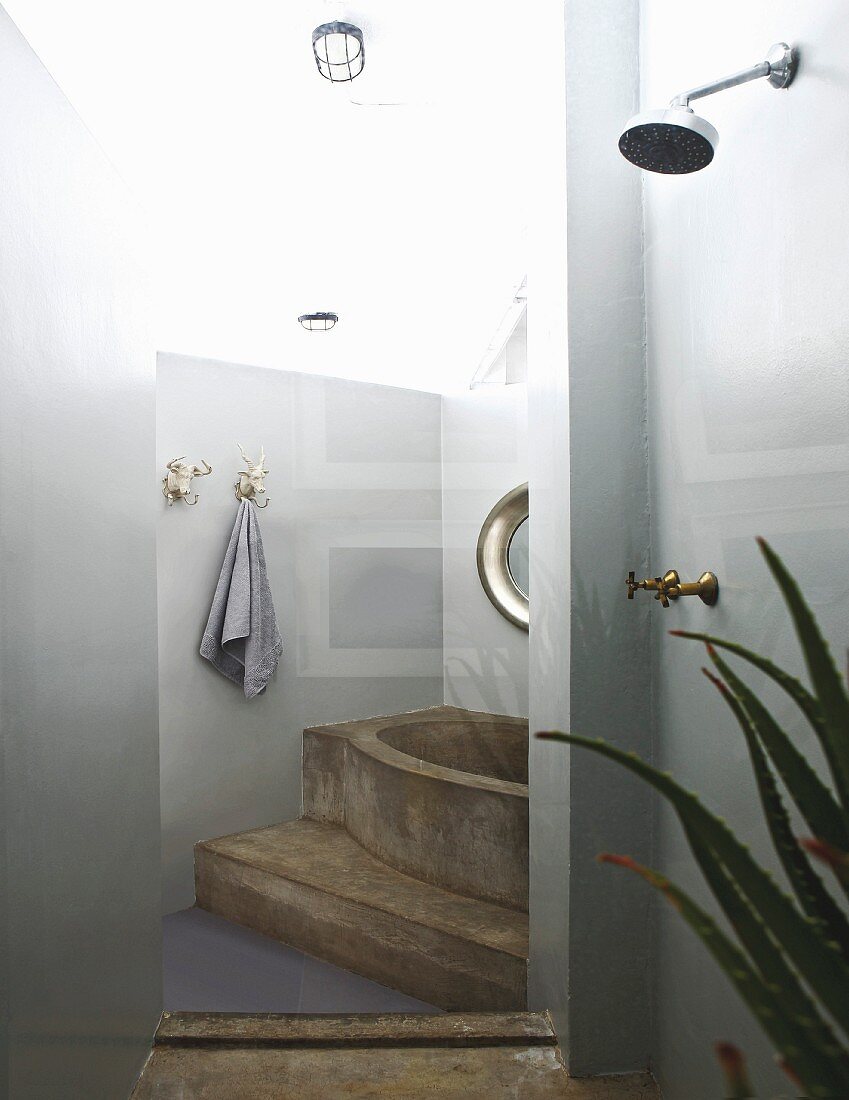 Moulded concrete bathtub on platform and shower area in foreground